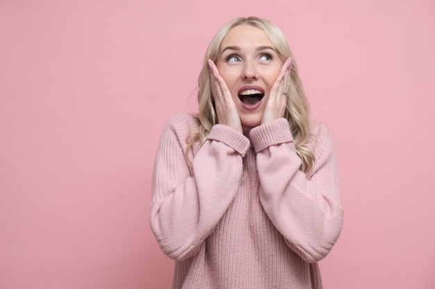 Foto bella donna felice sorpresa in maglione rosa sopra un rosa