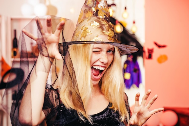 Beautiful surprised woman in witches hat and costume Halloween Woman portrait Halloween Witch with a carved Pumpkin and magic lights in a dark room Helloween people concept