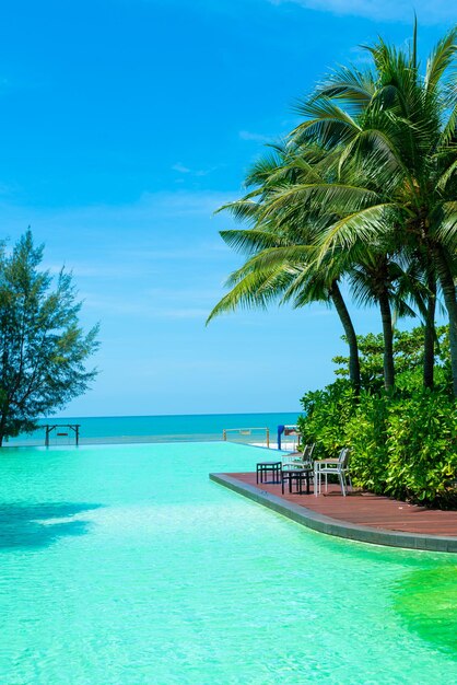 Beautiful swimming pool with coconut palm tree and sea background - holidays and vacation concept