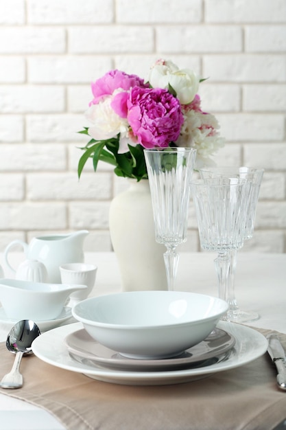 Beautiful table setting with flowers in vase on brick wall background