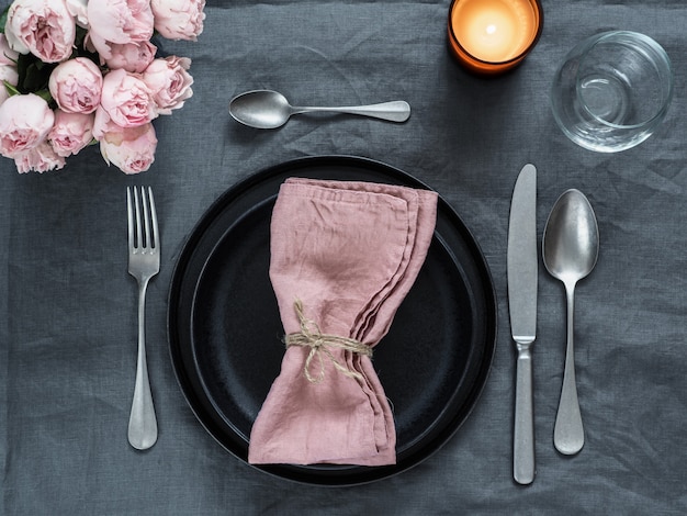 Beautiful table setting with pink spray roses and candle on gray linen tablecloth.