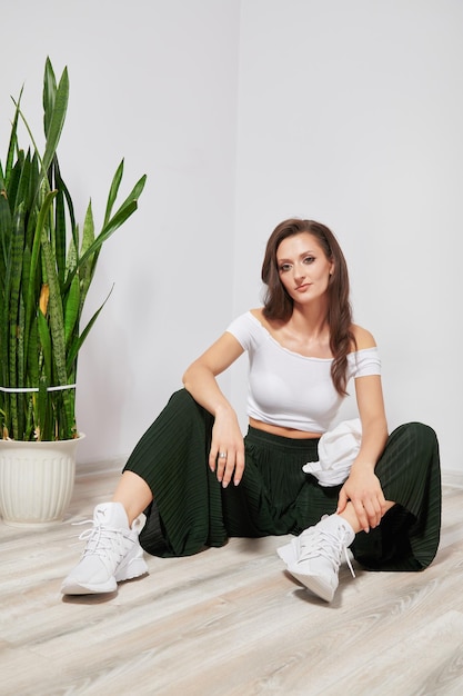 Beautiful tanned girl in stylish clothes posing on the floor