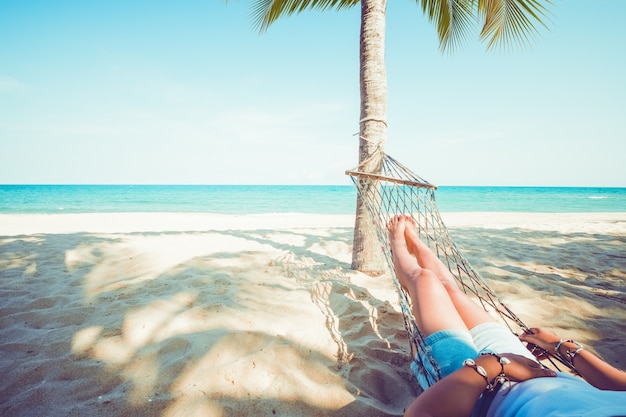 Beautiful tanned sexy woman sunbathes, relaxes and reads a book on hammock at sandy tropical beach