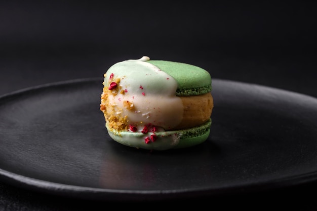 Beautiful tasty macaron with filling and fruit flavor on a black plate on a dark concrete background