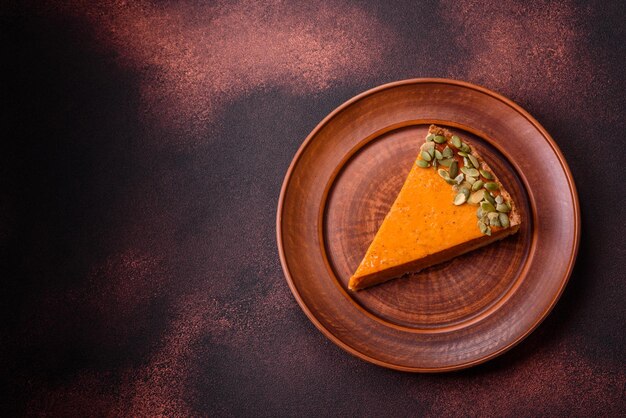 Beautiful tasty pumpkin pie with slices on a black ceramic plate on a dark concrete background