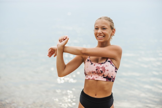 A beautiful teen girl is doing stretching exercise at the sea beach in summer sunny day.