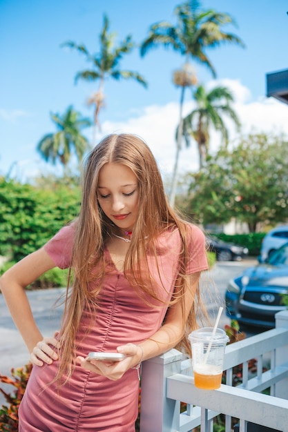 Beautiful teen girl using smartphone and drinking take away drink outdoor