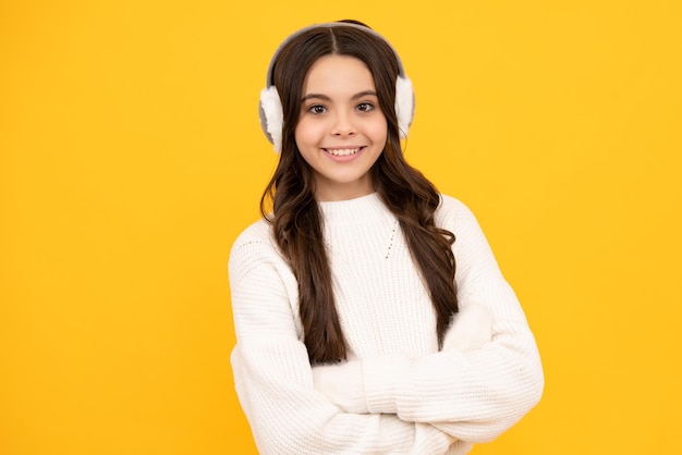 Beautiful teen girl in a winter warm earmuff earflaps and a warm sweater A child on a yellow isolated background