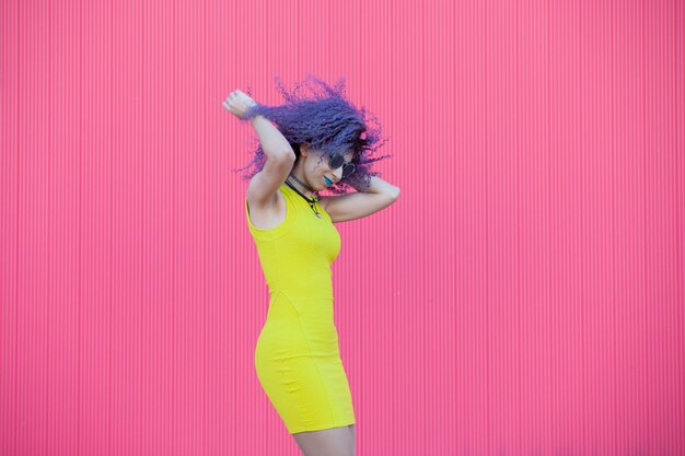 Beautiful teen woman with colored purple afro hair dancing on a pink wall