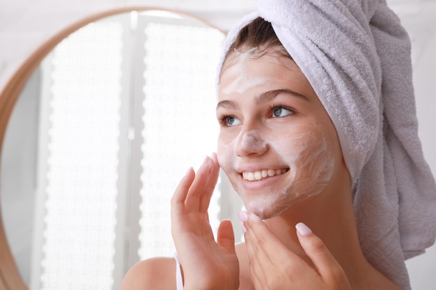 Beautiful teenage girl applying cleansing foam onto face in bathroom space for text Skin care cosmetic