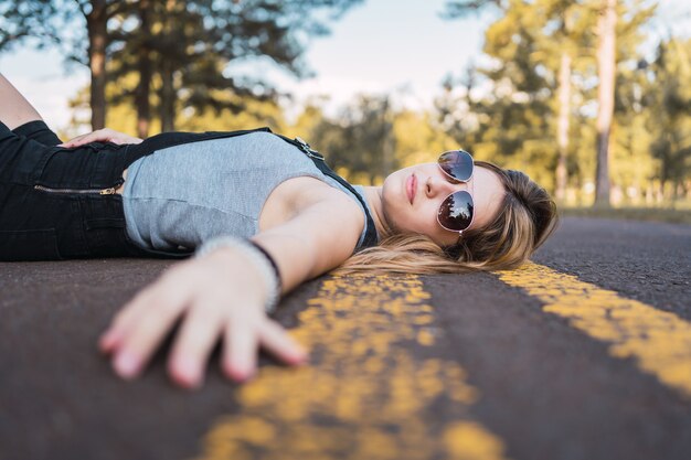 Foto bella ragazza adolescente sdraiata sulla strada con gli occhiali.