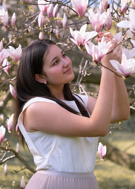 A beautiful teenage girl tenderly looks at magnolia flowers spring bloom