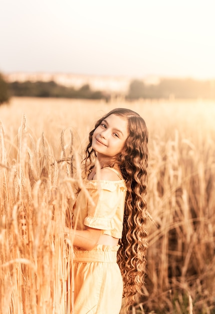 晴れた日に麦畑を歩いている長い髪の美しい10代の少女。屋外の肖像画。リラックスした女子高生