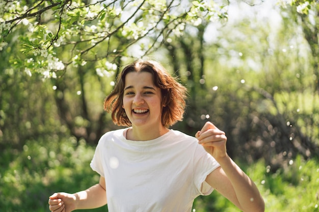 Beautiful teenage girl with spring flowers enjoying nature and laughing on spring garden Girl holding branch of an cherry tree Freedom and happiness concept Springtime