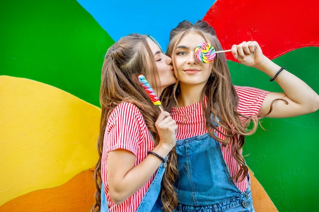 Beautiful teenage twin sisters kissed in colorful clothes with lollipops