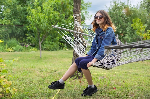 Beautiful teenager girl sitting resting in hammock in garden