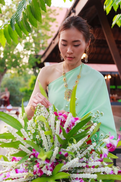 Beautiful Thai Asian woman in vintage Traditional Thai costume arranging flower vase.