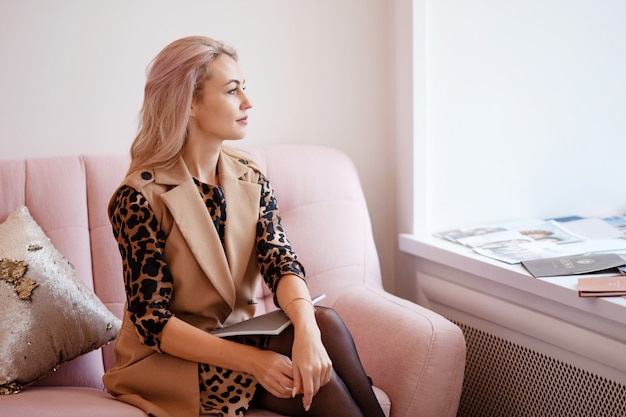 Beautiful thoughtful young woman siting on the sofa and looking out the window