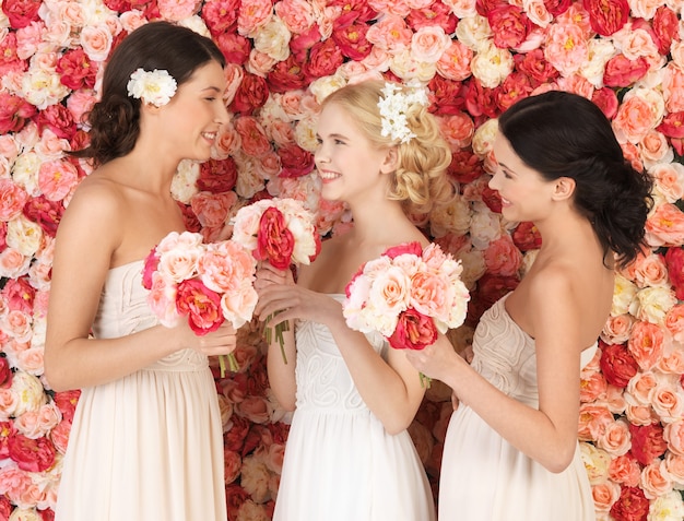 バラでいっぱいの背景を持つ美しい3人の女性