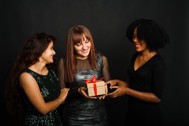 beautiful three young woman rejoicing while standing with present box isolated over black background