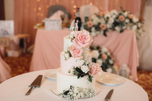 Photo beautiful threetiered wedding cake with a figurine and decorations of flowers in powdery tones