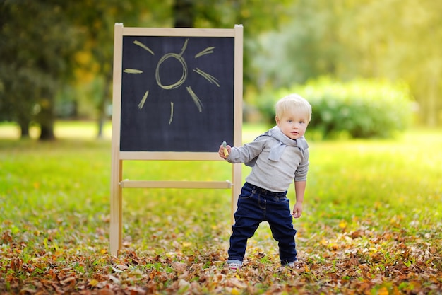 Bello disegno del ragazzo del bambino che fa una pausa una lavagna all'aperto