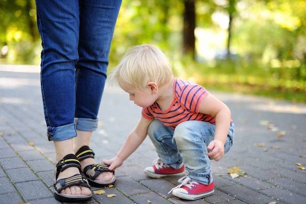 Beautiful toddler boy playing with footwear at sunny park