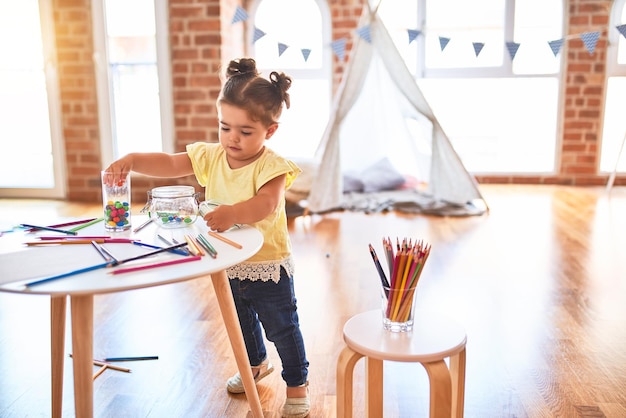 Beautiful toddler standing playing with chocolate colored balls on the table at kindergarten