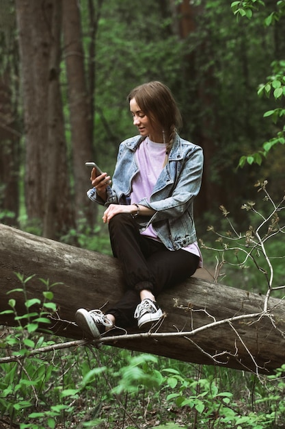 beautiful tourist girl in casual clothes in a green forest on a walk looking through the phone