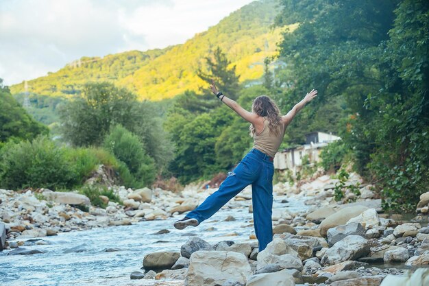 a beautiful tourist girl enjoys life near a mountain river on the  background she has mountains