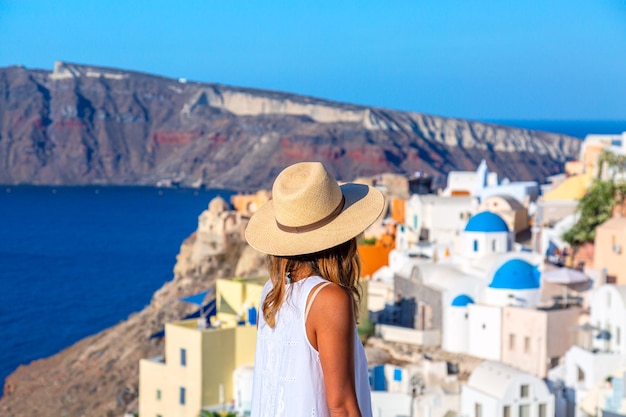 Foto bella ragazza turistica con cappello di paglia contro il villaggio di oia con famose case bianche e chiese blu sull'isola di santorini mar egeo grecia concetto di viaggio