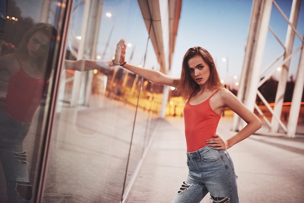 Beautiful  tourist girl walking in busy city street near the airport. Woman looking at camera outdoors wearing fashionable red t-shirt.