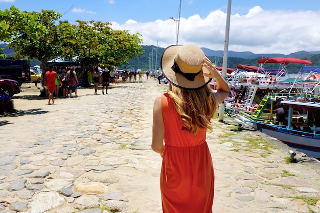 Beautiful tourist woman walking on harbor where to travel by ferry or rented boat or yacht to explore warm tropical destinations