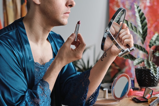 Beautiful transgender man applying lipstick feeling comfortable in female makeup