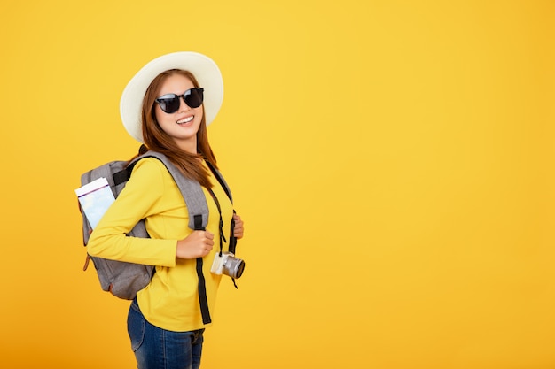 Donna asiatica del bello viaggiatore con la macchina fotografica su fondo giallo