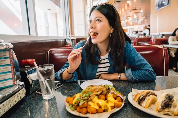 beautiful traveler experience American culture. young girl eating American food and sitting in American restaurant. diner in LA concept.