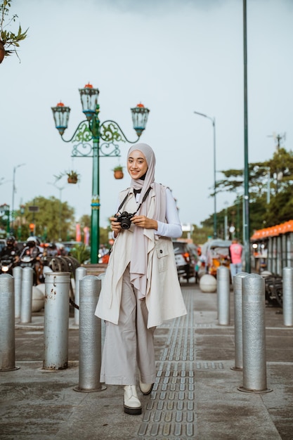 Красивый путешественник в хиджабе держит камеру во время прогулки по тротуару