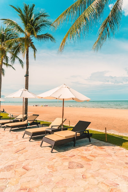 旅行や休暇のためのホテルリゾートのスイミングプールの周りの傘と椅子のある美しい熱帯のビーチと海