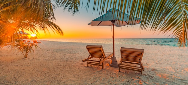 Красивый тропический закат, пара шезлонгов, шезлонгов, зонтик под пальмовыми листьями, белый песок, море
