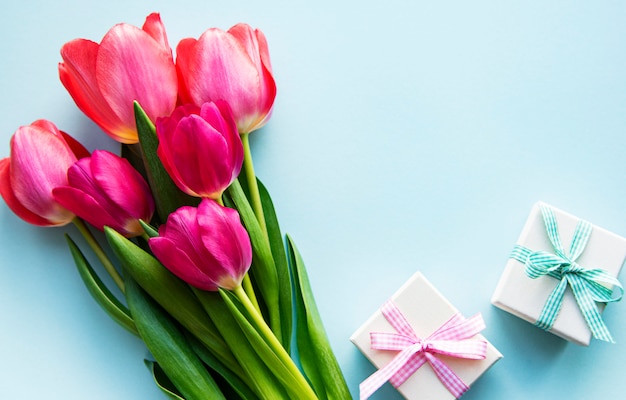 Beautiful tulips bouquet and gift boxes on blue background