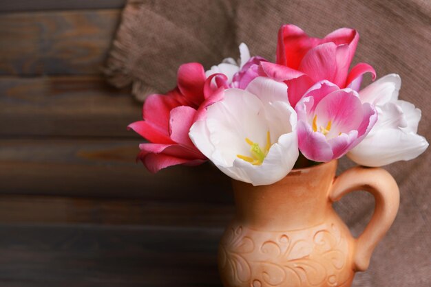 Beautiful tulips in bucket in pitcher on table on grey background