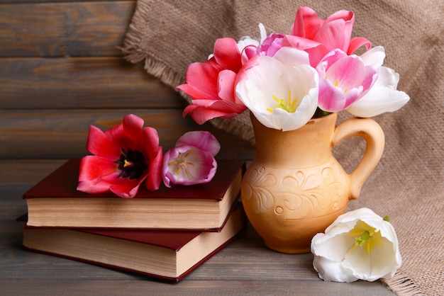 Beautiful tulips in bucket in pitcher on table on grey background