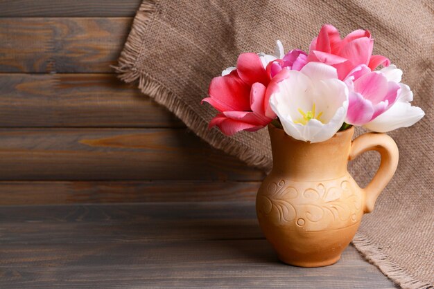 Красивые тюльпаны в ведре в кувшине на столе на сером фоне