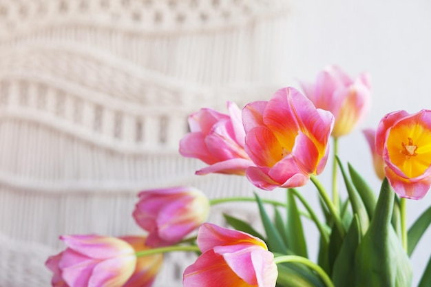 Beautiful tulips Cozy interior of living room with flowers in vase macrame decor Minimalistic concept of home decor Stylish macrame wall hanging on the white wall