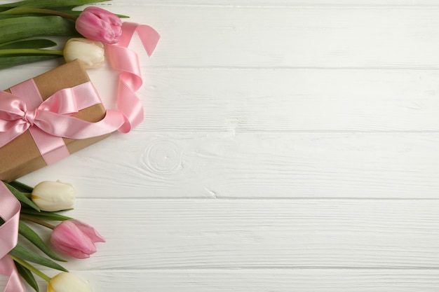 Beautiful tulips and gift box on white wooden background