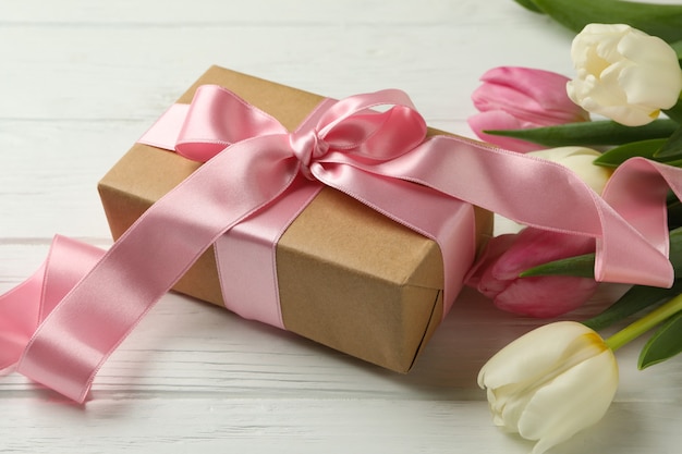Красивые тюльпаны и подарочная коробка на белом деревянном фоне
