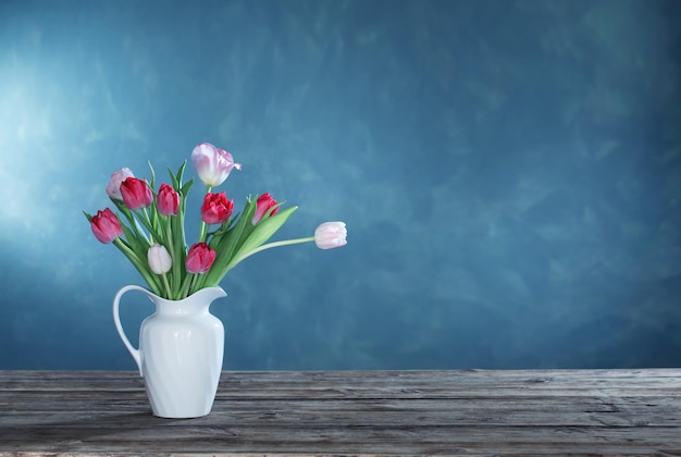 Beautiful tulips in white jug on dark background