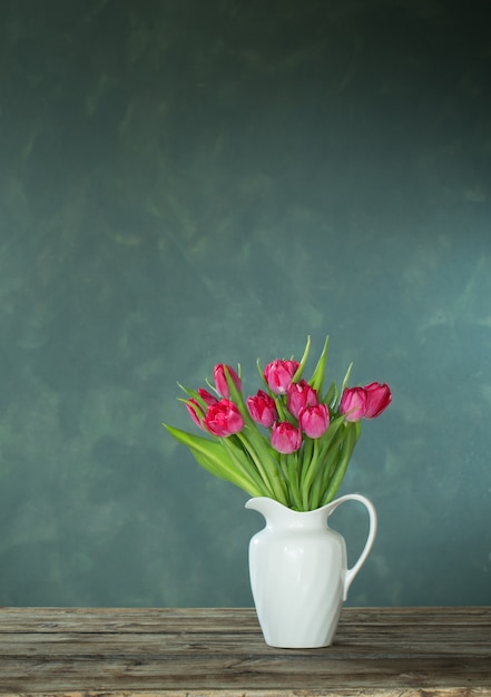 Bei tulipani in brocca bianca su sfondo scuro