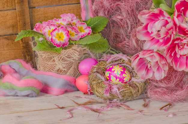 Beautiful tulips with colorful eggs in nest on wooden background Composition with Easter eggs and blooming flowers