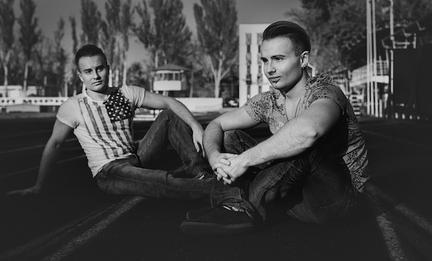 Photo beautiful twin brothers posing in the street, sitting on the pavement. black and white. summer evening